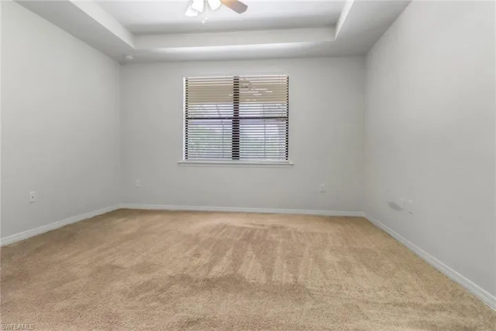 Unfurnished room with light carpet, a tray ceiling, and a ceiling fan