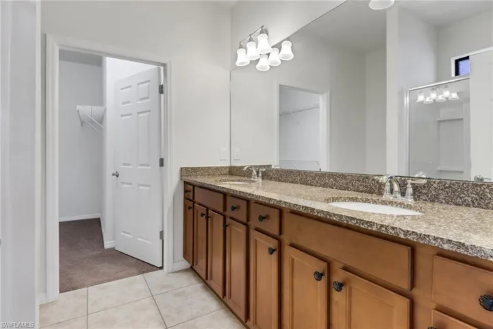 Full bath with double vanity, a walk in closet, and tile patterned flooring