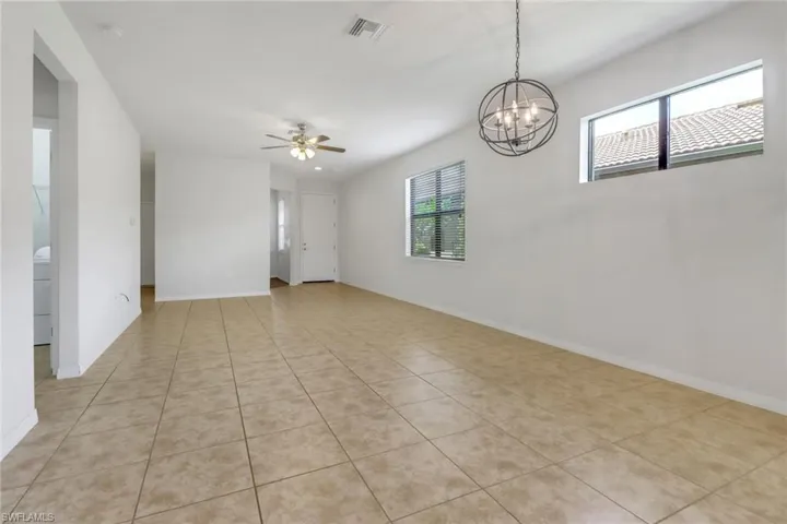 Empty room featuring ceiling fan, light tile patterned flooring, a smoke detector, and a chandelier