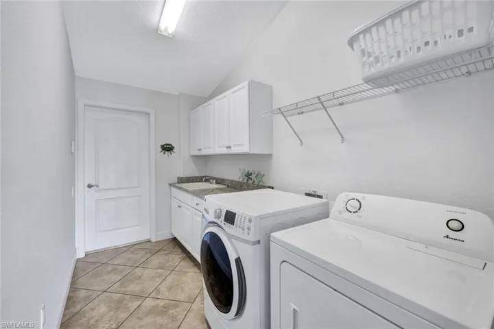 Clothes washing area featuring independent washer and dryer, sink, light tile floors, and cabinets
