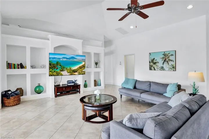 Living room featuring high vaulted ceiling, built in shelves, light tile flooring, and ceiling fan