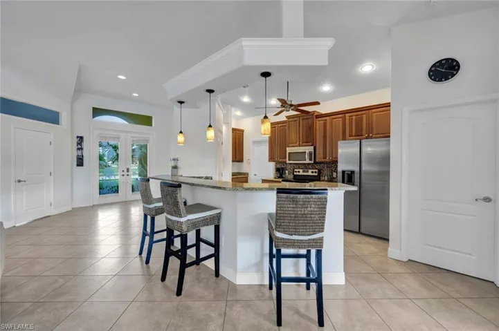 Kitchen featuring stainless steel appliances, light stone counters, decorative light fixtures, backsplash, and ceiling fan
