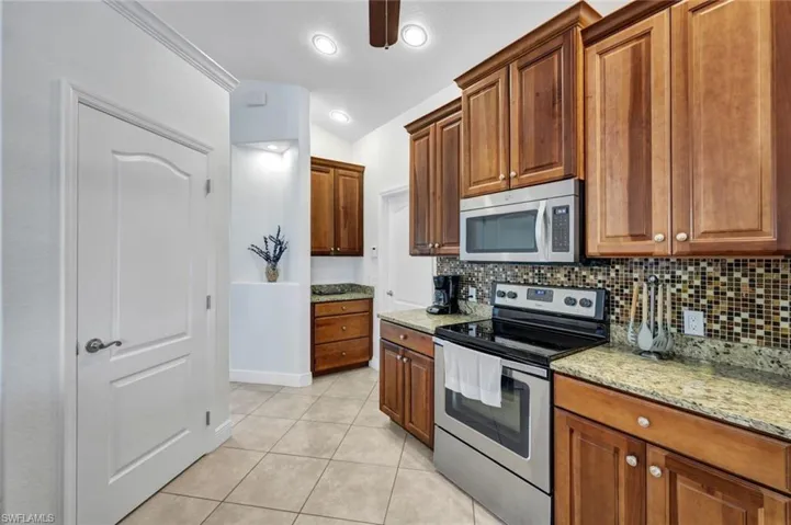 Kitchen with lofted ceiling, backsplash, light stone counters, and stainless steel appliances