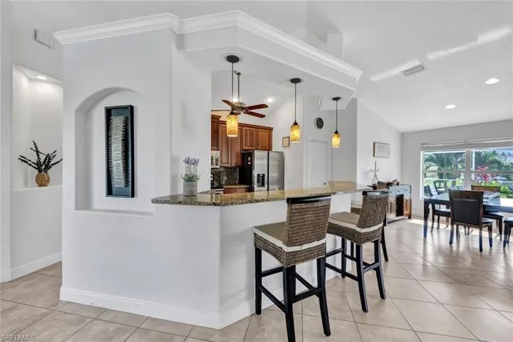 Kitchen with ceiling fan, kitchen peninsula, stainless steel fridge, stone counters, and backsplash
