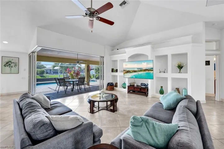 Tiled living room with built in features, ceiling fan, and high vaulted ceiling