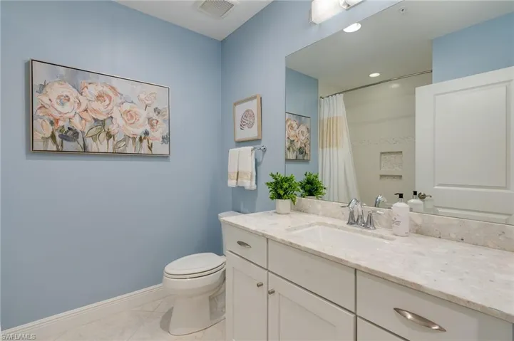 Guest bathroom features neutral colors, a custom raised shower head to accommodate a tall person, and a corresponding oversized custom length shower curtain and recessed lighting