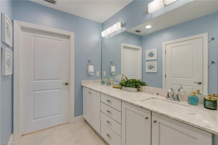 Primary bathroom featuring a double sink vanity and bright vanity lights as well as flush ceiling lighting.  Ample storage and lower cabinets feature pull out stainless organizers.