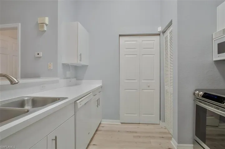 Kitchen with white cabinets, sink, white appliances, and light wood-type flooring