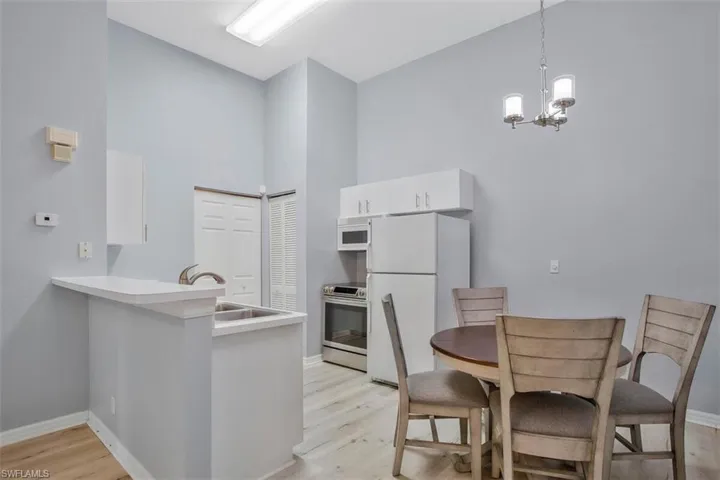 Kitchen with white cabinetry, white appliances, high vaulted ceiling, and light hardwood / wood-style flooring
