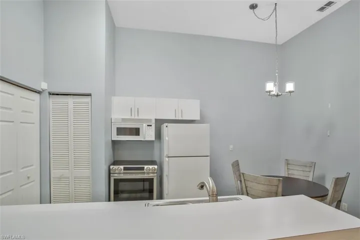 Kitchen with white appliances, decorative light fixtures, sink, white cabinetry, and a chandelier