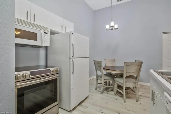 Kitchen featuring decorative light fixtures, an inviting chandelier, light hardwood / wood-style floors, white cabinetry, and white appliances