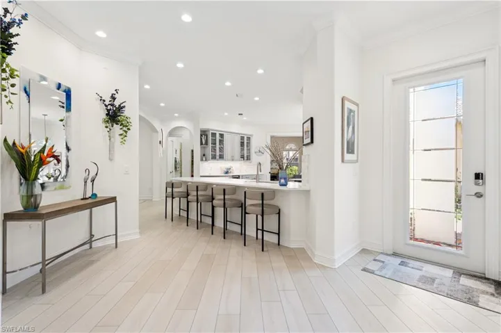 Kitchen featuring a kitchen breakfast bar, a peninsula, arched walkways, glass insert cabinets, and light wood-type flooring