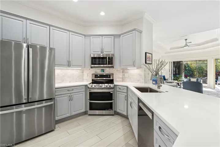 Kitchen with stainless steel appliances, gray cabinets, crown molding, light stone counters, and a ceiling fan