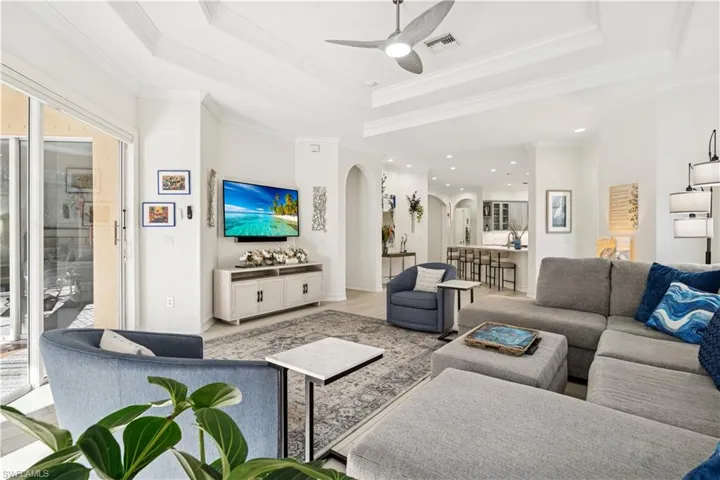 Living room featuring a ceiling fan, a tray ceiling, arched walkways, and crown molding