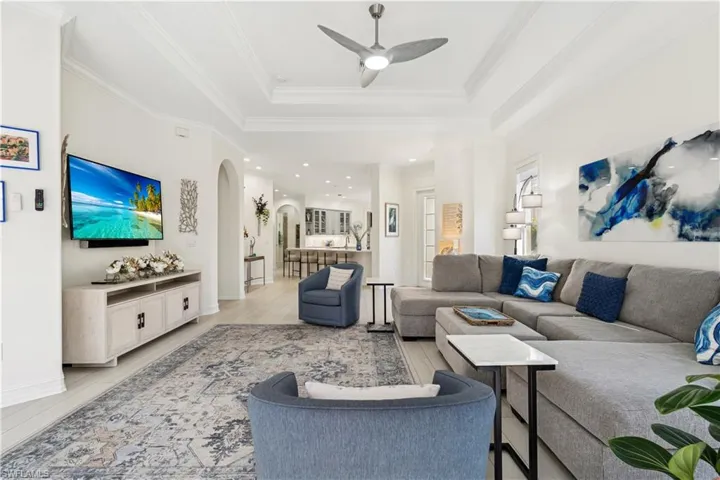 Living area with a ceiling fan, light wood-type flooring, arched walkways, a raised ceiling, and crown molding