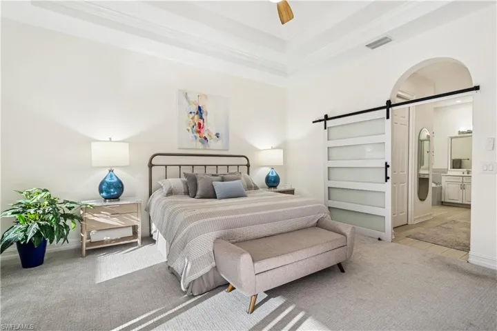 Bedroom featuring a barn door, a ceiling fan, connected bathroom, ornamental molding, and a tray ceiling