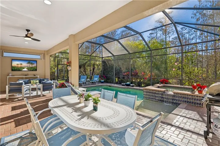 View of patio / terrace with an outdoor living / dining area, glass enclosure, a pool with connected hot tub, a ceiling fan, and grilling area
