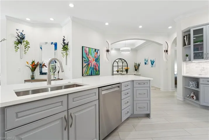 Kitchen with gray cabinets, open shelves, stainless steel dishwasher, light stone countertops, and arched walkways