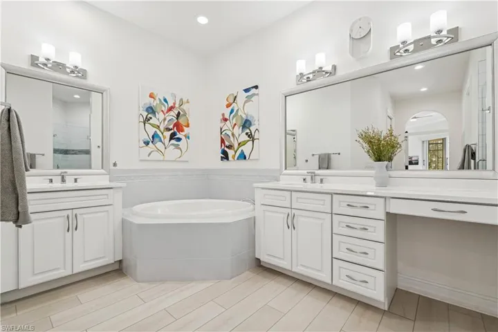Bathroom featuring two vanities, a stall shower, a garden tub, wood tiled floors, and recessed lighting