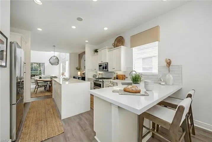 Kitchen with high quality appliances, a breakfast bar area, white cabinetry, a peninsula, and hanging light fixtures