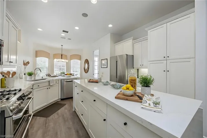 Kitchen featuring stainless steel appliances, white cabinets, dark wood finished floors, and decorative light fixtures
