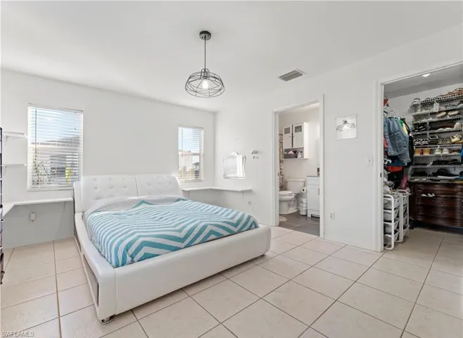Bedroom with a walk in closet, light tile patterned flooring, a closet, and ensuite bath