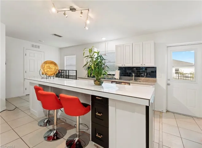 Kitchen with light countertops, light tile patterned flooring, decorative backsplash, white cabinetry, and a kitchen island