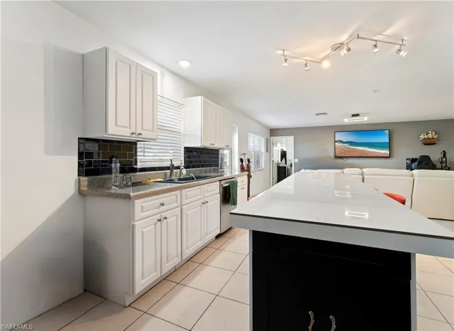 Kitchen with stainless steel dishwasher, a center island, open floor plan, light tile patterned flooring, and backsplash