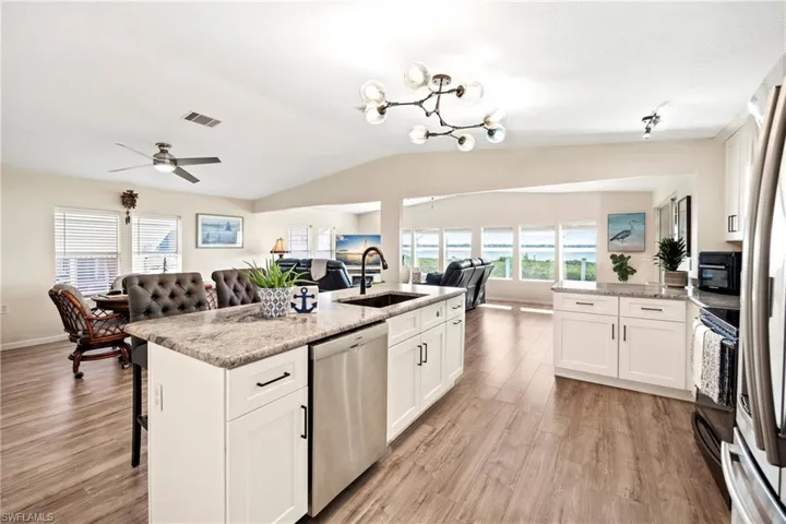 Kitchen featuring open floor plan, white cabinets, a kitchen breakfast bar, light stone counters, and stainless steel appliances