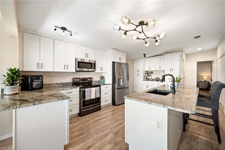 Kitchen with a breakfast bar, appliances with stainless steel finishes, light stone counters, and white cabinets