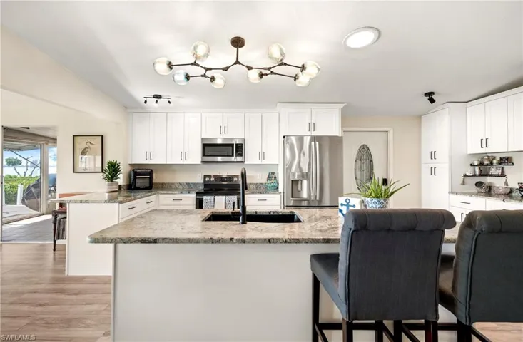 Kitchen featuring appliances with stainless steel finishes, white cabinets, light stone countertops, light wood-type flooring, and a peninsula