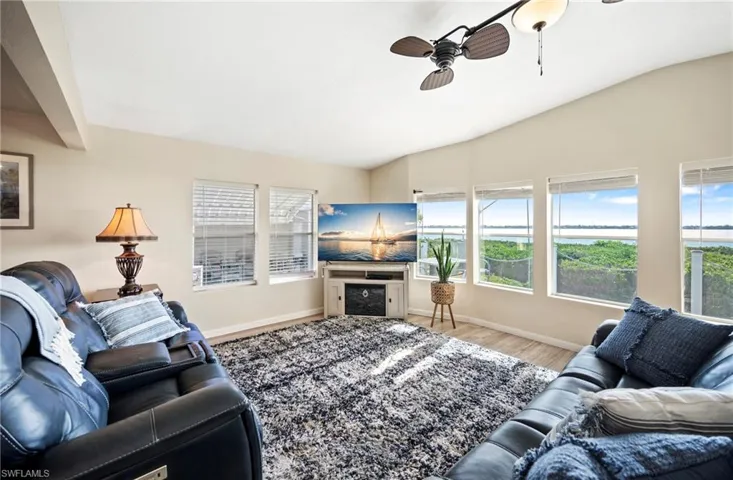 Living area with vaulted ceiling, wood finished floors, a ceiling fan, and healthy amount of natural light