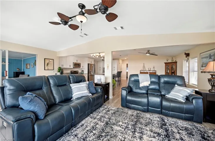 Living room featuring a ceiling fan, wood finished floors, vaulted ceiling, and a chandelier