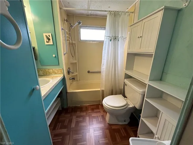 Full bathroom featuring vanity, toilet, shower / bath combo, and parquet flooring