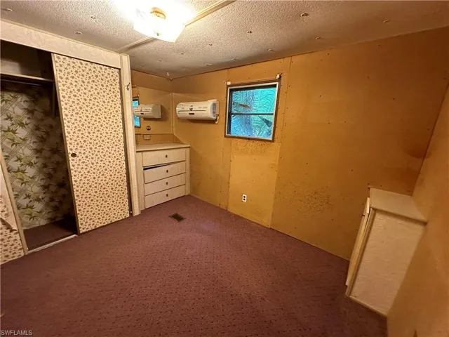 Unfurnished bedroom with a closet, carpet, a wall unit AC, and a textured ceiling