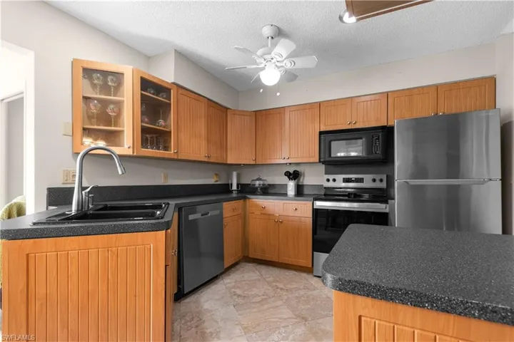 Kitchen with stainless steel appliances, dark countertops, glass insert cabinets, ceiling fan, and a textured ceiling