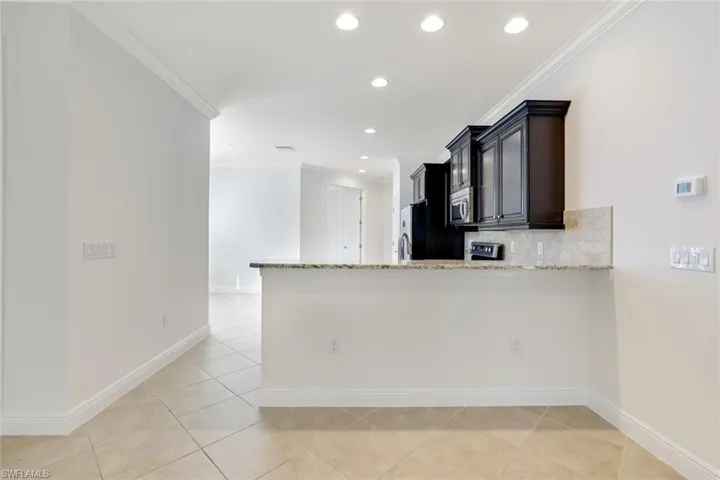Kitchen featuring ornamental molding, light stone counters, backsplash, dark cabinets, and light tile patterned flooring