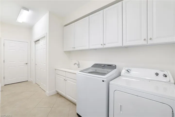 Laundry area with light tile patterned floors, washing machine and dryer, and cabinet space