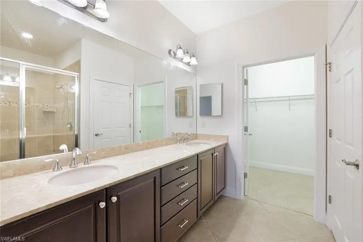Full bathroom with a shower stall, double vanity, light tile patterned flooring, and a spacious closet