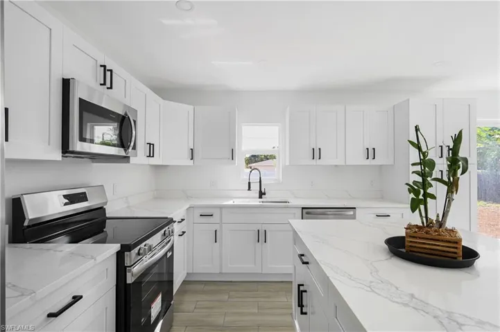 Kitchen featuring stainless steel appliances, white cabinets, light stone counters, and wood tiled floors