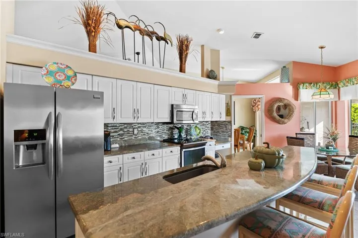Kitchen with appliances with stainless steel finishes, a kitchen bar, granite counters, and white cabinetry