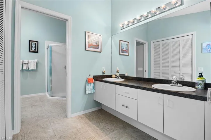 Bathroom featuring a closet, double vanity, a shower stall, and light tile patterned flooring