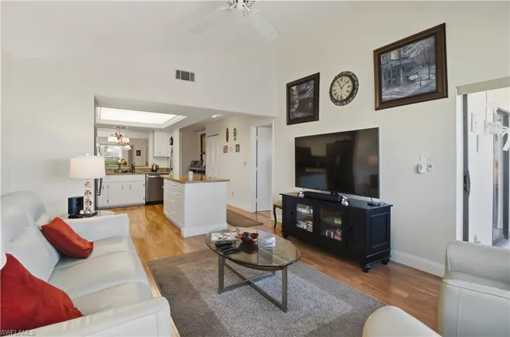 Living room featuring light wood-type flooring, a ceiling fan, lofted ceiling, and a chandelier