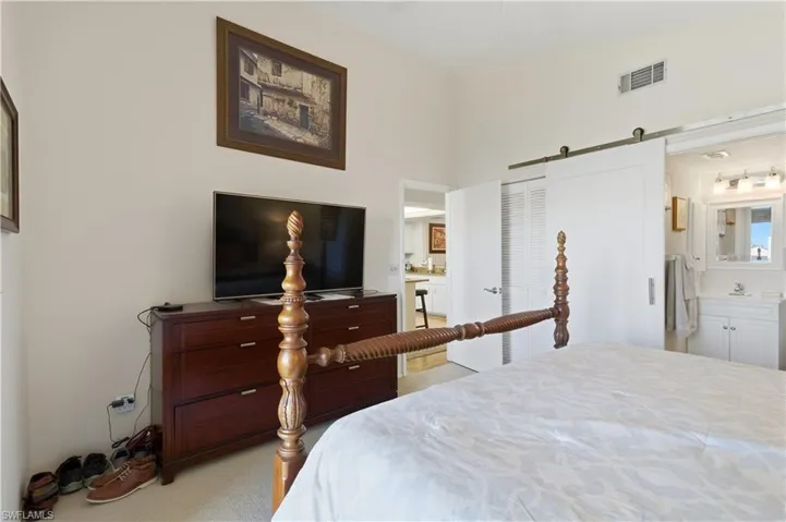 Bedroom with a barn door, a closet, ensuite bathroom, and light colored carpet