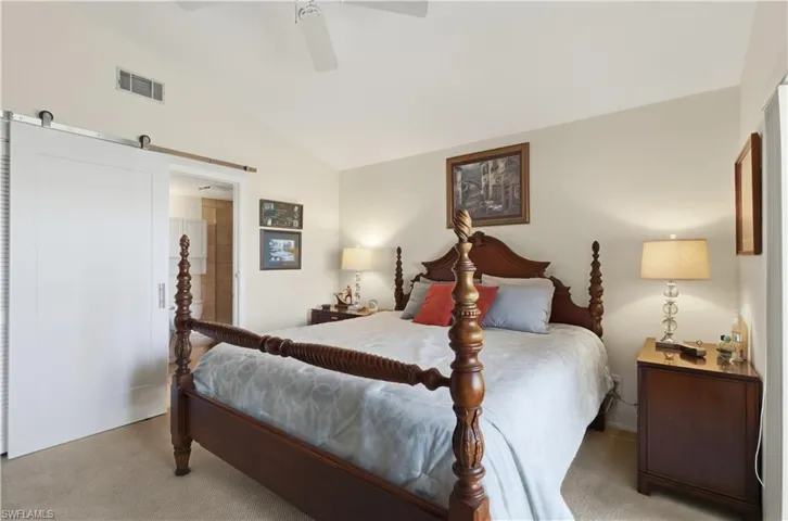 Bedroom with lofted ceiling, a barn door, light carpet, and ceiling fan