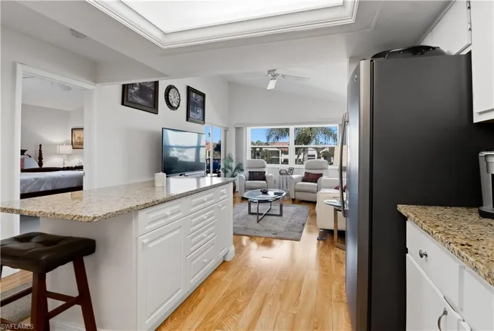 Kitchen featuring white cabinetry, open floor plan, light stone counters, and vaulted ceiling