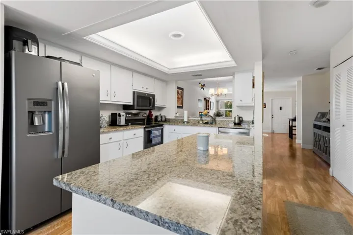 Kitchen with appliances with stainless steel finishes, white cabinetry, a chandelier, a raised ceiling, and light wood-style floors