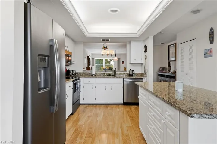Kitchen featuring white cabinetry, appliances with stainless steel finishes, a chandelier, light stone counters, and light wood-style flooring