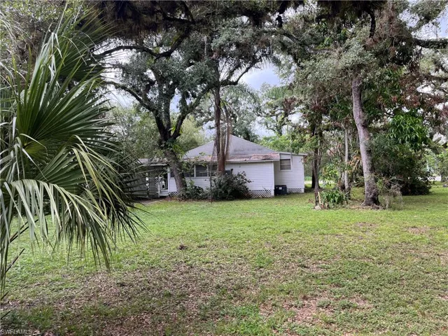 Expansive rear yard featuring a large white-sided residence with multiple windows, mature trees, and a screened porch