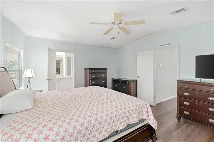Wood-finish flooring with light blue wall panels, vaulted ceiling with a ceiling fan, and access to a vanity space